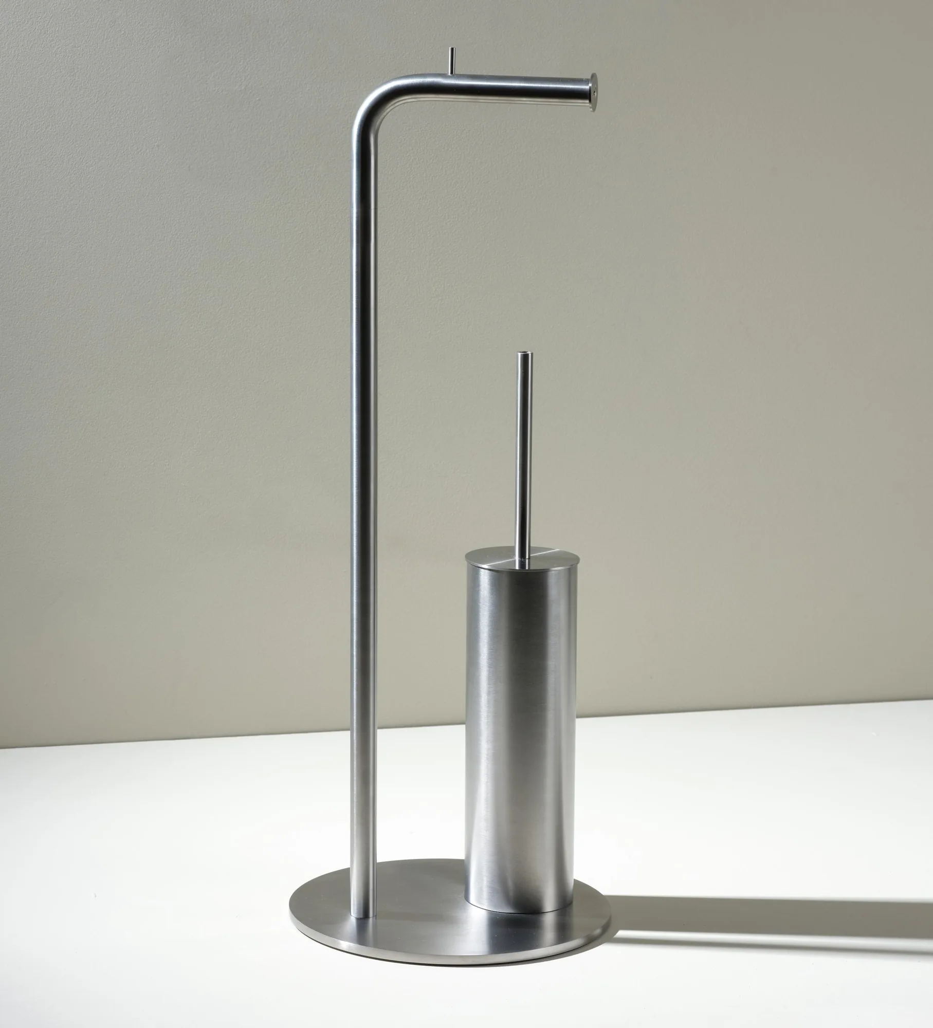 Freestanding stainless steel toilet roll and brush holder unit on a single floor-standing stand